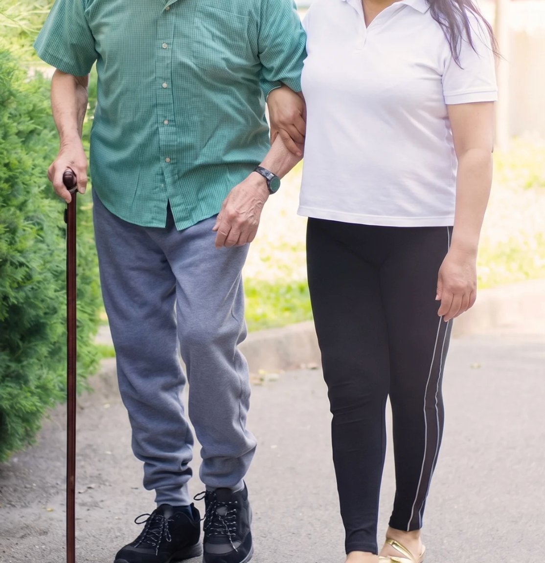 Betreuerin geht Arm in Arm mit einem älteren Mann spazieren